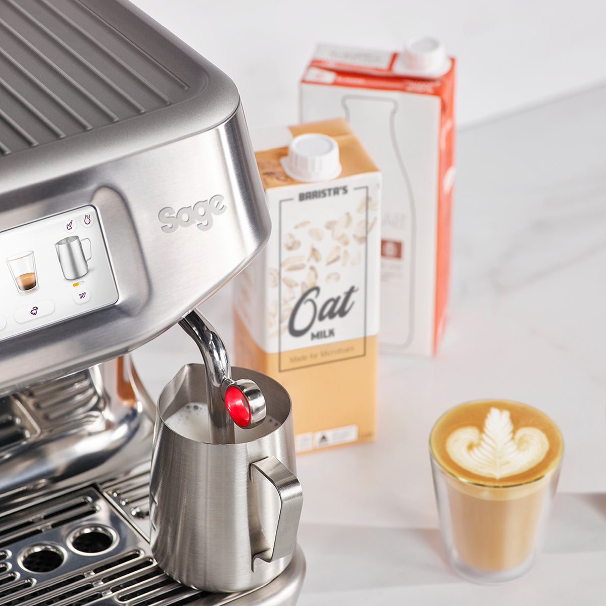 The Barista Touch Impress automatic steam wand texturing a jug of oat milk, with a finished flat white beside it, official Sage photography