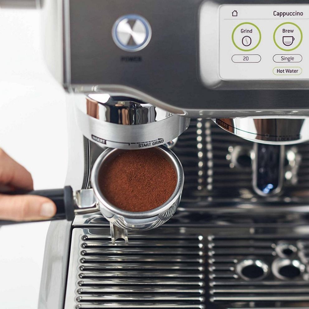 A freshly ground and tamped 58 mm portafilter under the Oracle Touch grinder, official Sage photography
