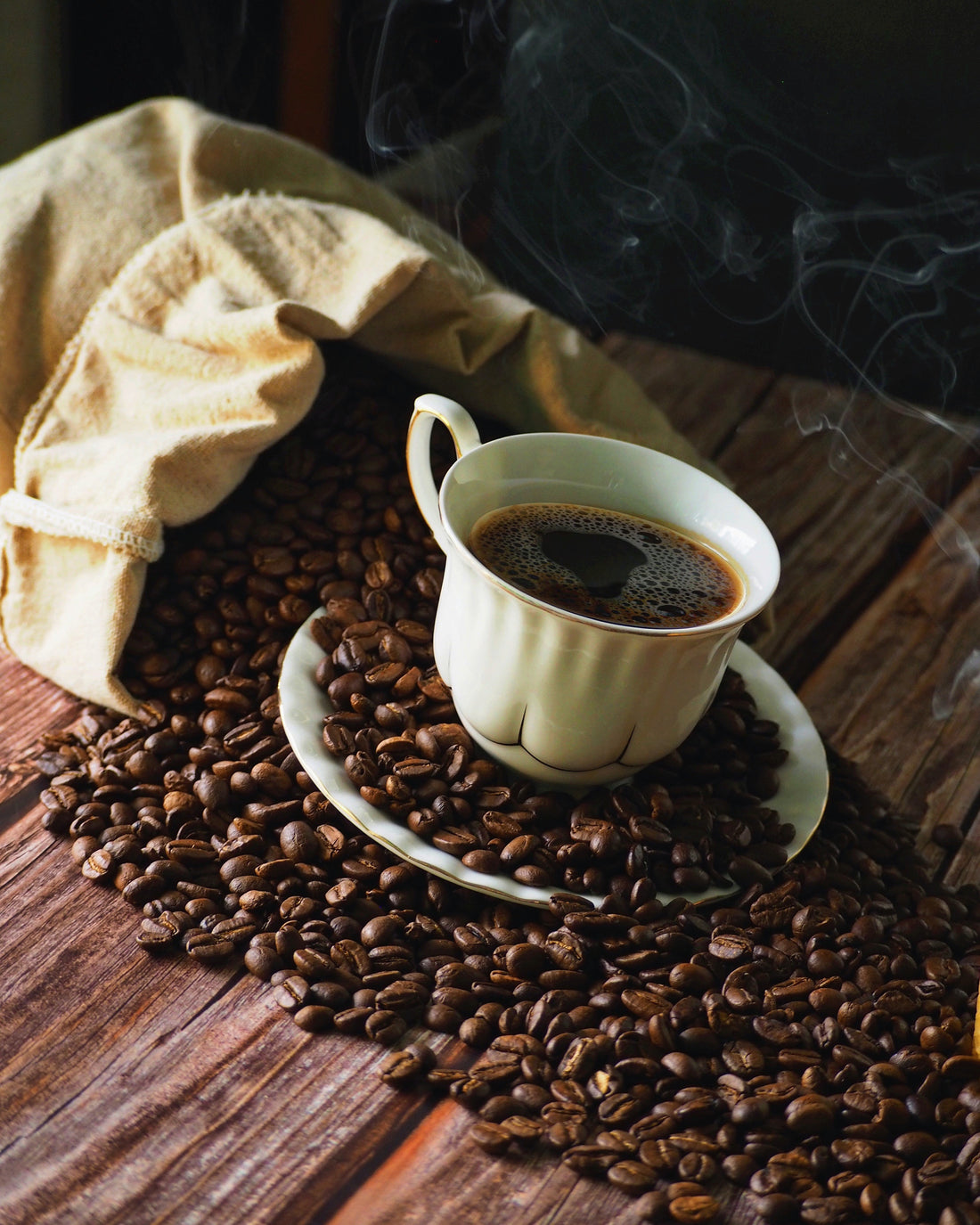 image of hot coffee in a cup over  a bag of spilled roasted beans 